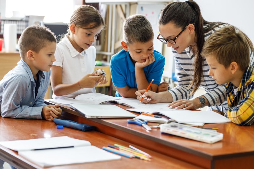 groupe d'enfants autour d'une enseignante leur expliquant un point.