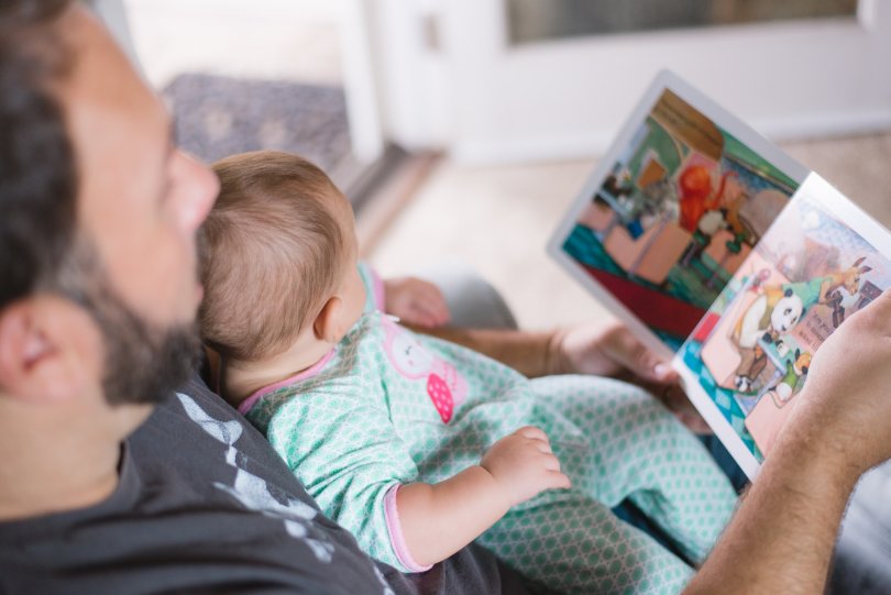 Un enfant sur les genoux de son père qui lit un livre