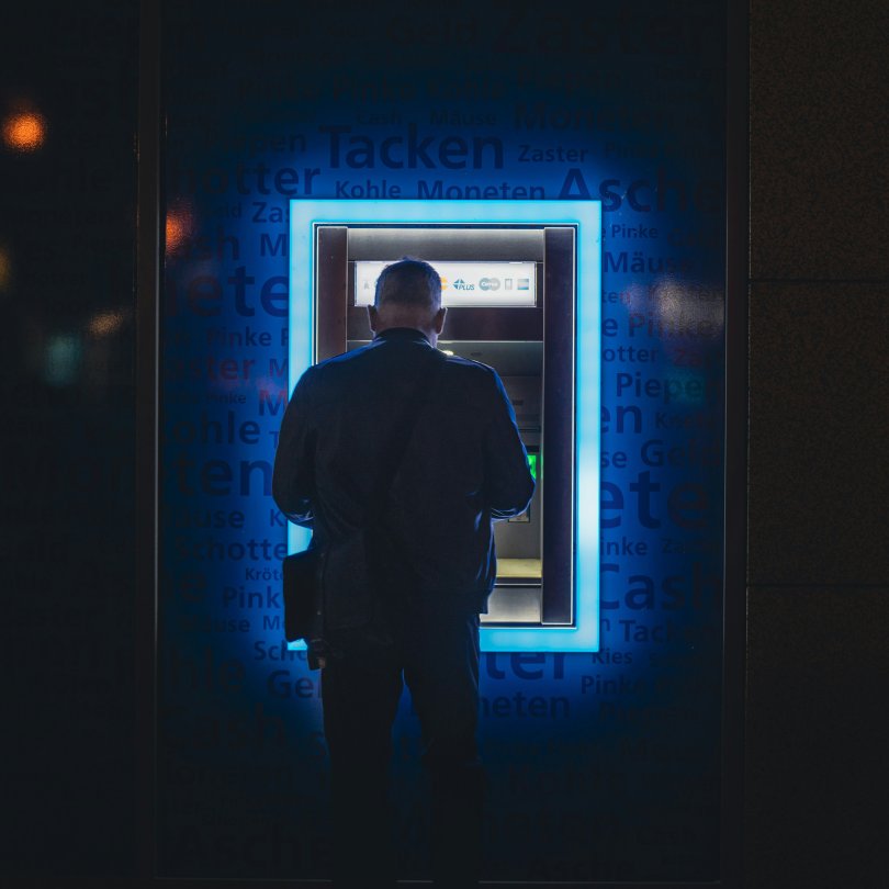 Homme de dos retirant, en pleine nuit, de l'argent à un distributeur de billets