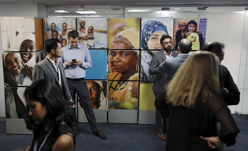 groupe d'hommes et de femmes d'origines diverses devant un mur avec des photos de femmes.