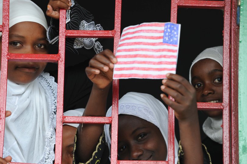 Groupe d'enfants dont l'un tient le dessin d'un drapeau américain par la fenêtre d'une salle de classe lors d'une cérémonie d'inauguration de l'école primaire de Nioumamilima.