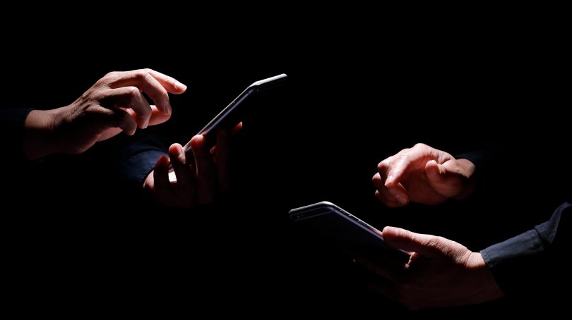 Deux paires de mains éclairées sur fond noir utilisent chacune un téléphone