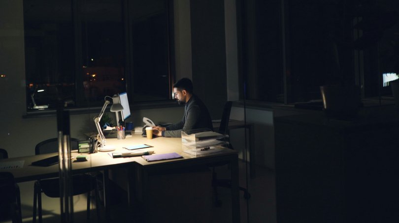 Un homme travaillant seul dans un bureau vide, lumières éteintes. Photo: Vitaly Gariev