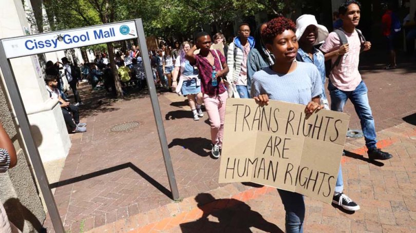 A person is holding a sign that reads ‘Trans Rights are Human Rights’. 