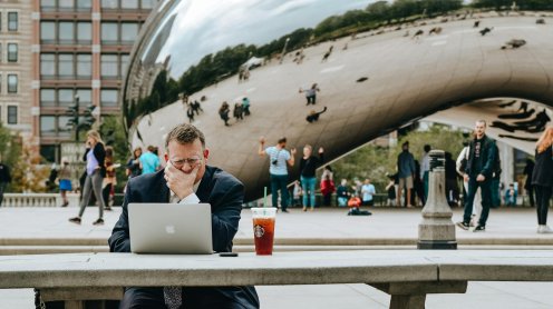 Un homme en tenue de ville travaillant sur son ordinateur assis à une table de pique nique en face de la "Bean" de New-York. Photo : Tim Gouw via Pexels