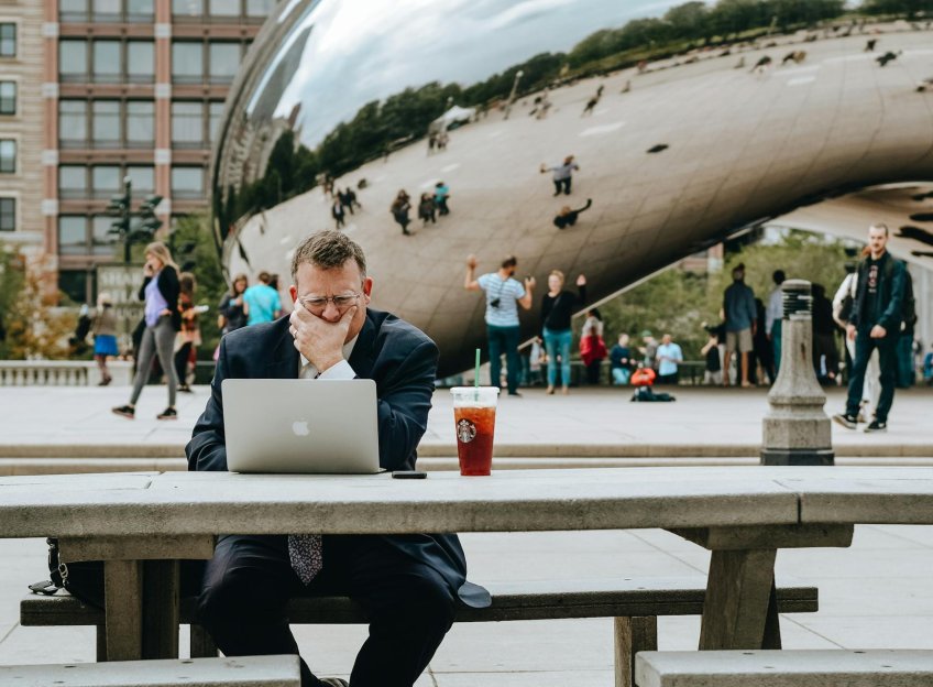 A man in business attire, working on his laptop and sitting on a public bench nearby the Cloud Gate in Chicago. Picture: Tim Gouw via Pexels